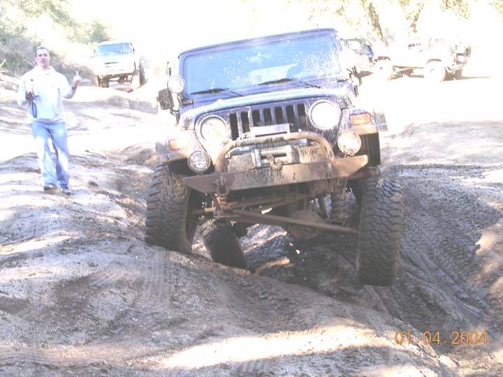 Blue lifted Jeep Wrangler with winch bumper crawling a rutted dirt trail