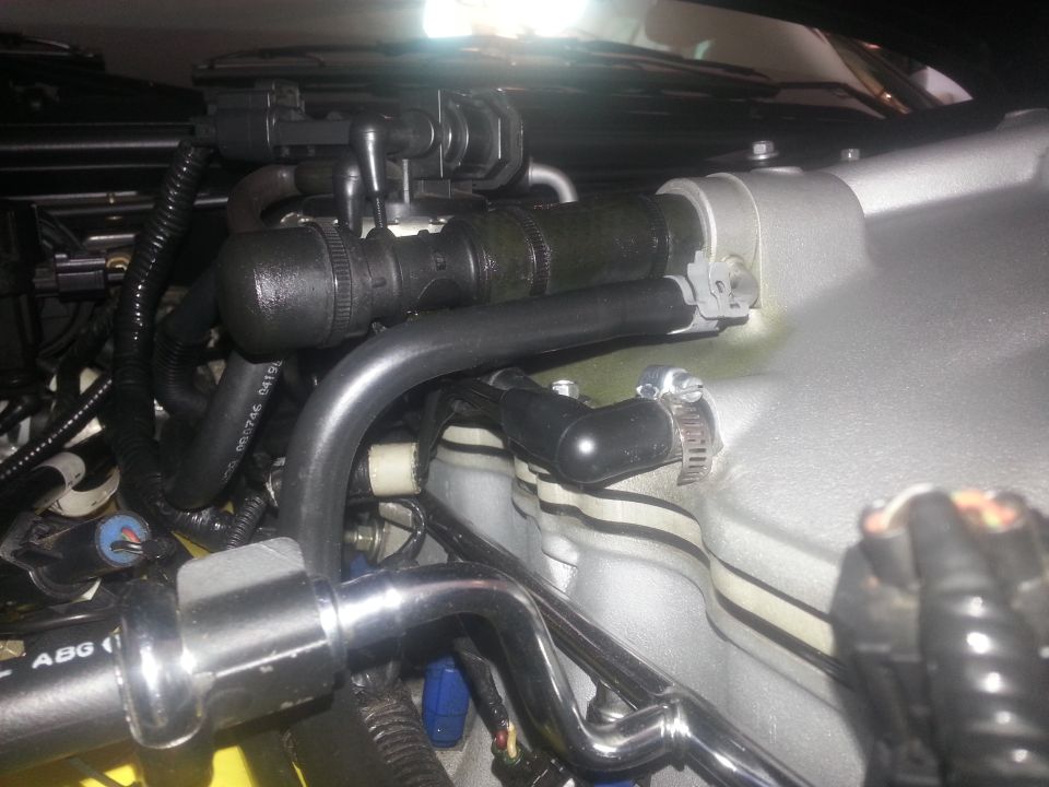 Close-up of engine bay with various hoses, clamps, and metal components. Some hoses have text on them