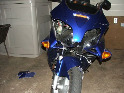 2006 Honda Reflex - A blue motorcycle sits with its front fairing heavily damaged, revealing internal components. Loose blue body panels are scattered on the f…