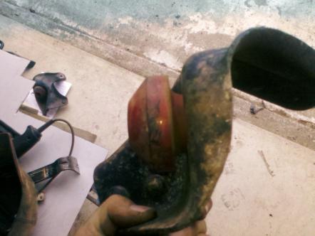 1982 Ford Bronco - A close-up of a rusty vehicle part with a red lens, held by a hand, with a website logo in the corner.