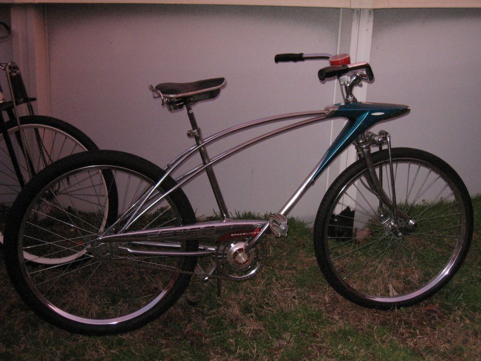 Chrome cruiser bicycle with teal front fairing and wide rear tire. Another bicycle is partially visible behind it