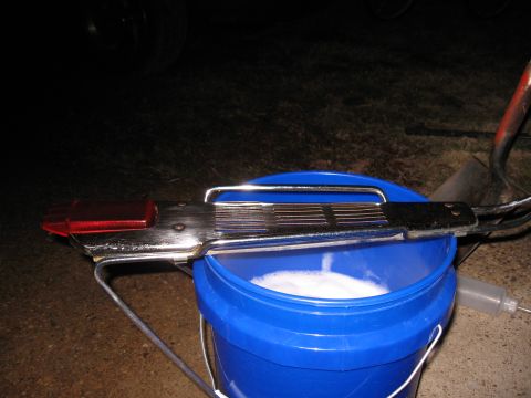 Chrome tail light assembly with red lens and ribbed handle over a blue bucket of soapy water