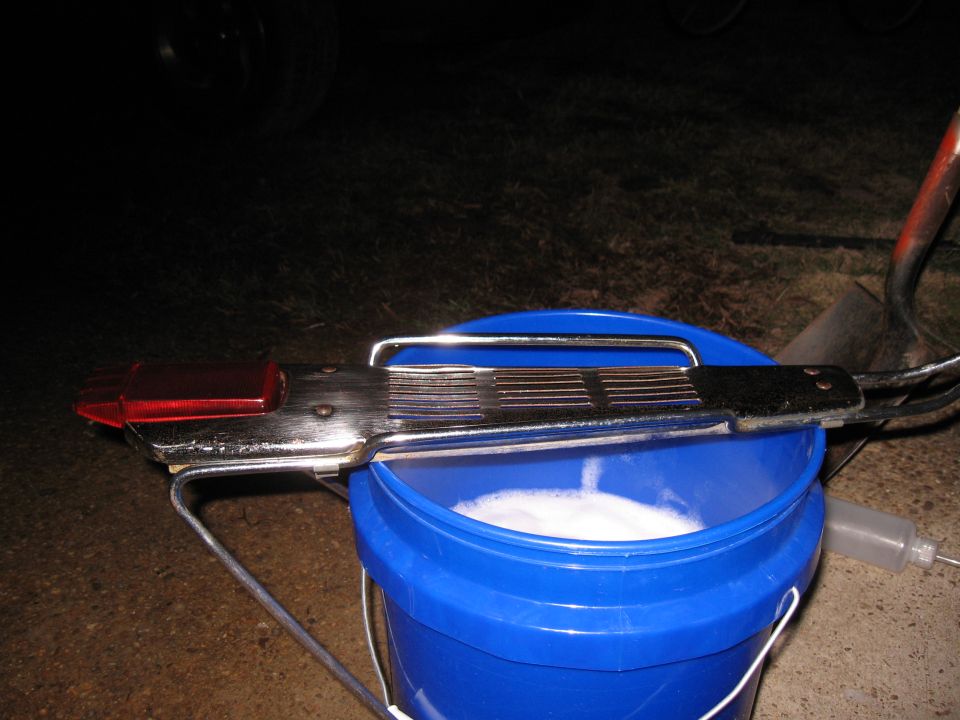Chrome tail light assembly with red lens and ribbed handle over a blue bucket of soapy water