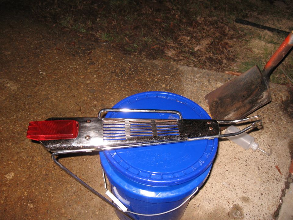 Chrome tail light assembly with red lens resting on a blue bucket next to a shovel