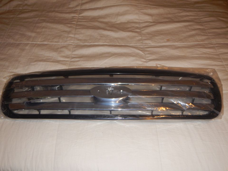 Front view of black-edged chrome-bar grille with Ford oval, wrapped in plastic on a white sheet