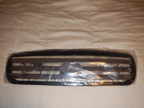 2003 Ford Crown Victoria - black-and-chrome horizontal-bar front grille with a central oval emblem, plastic-wrapped on a white cloth.