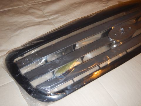 2003 Ford Crown Victoria - Angled close-up of a glossy black-and-chrome bar grille with a Ford oval mount, seen through plastic wrap.