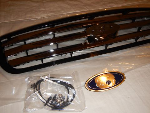 2003 Ford Crown Victoria - Angled chrome-bar grille beside a hardware bag and a gold-rimmed blue Ford oval emblem on a white sheet.