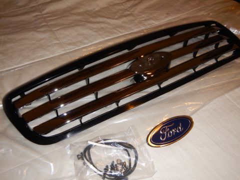 2003 Ford Crown Victoria - black-and-chrome grille with loose screw hardware and a gold-trimmed blue Ford oval emblem on a white sheet.