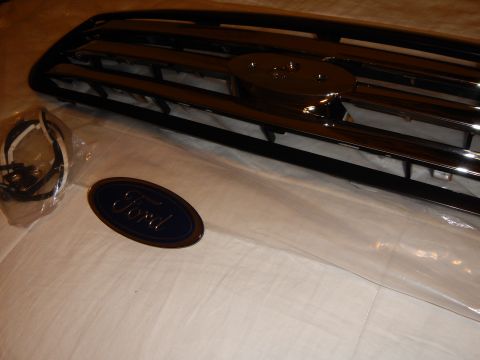 2003 Ford Crown Victoria - Angled chrome-bar grille with a hardware bag and a blue Ford oval emblem placed in the foreground.
