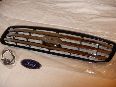 2003 Ford Crown Victoria - black-and-chrome bar grille with mounting hardware and a blue Ford oval emblem laid out on a white sheet.
