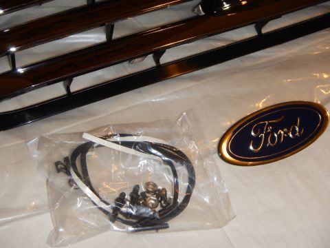 2003 Ford Crown Victoria - plastic bag of grille mounting screws and clips beside a gold-rimmed blue Ford oval emblem on white cloth.
