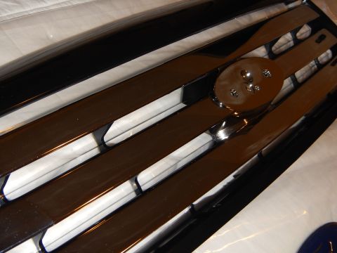 2003 Ford Crown Victoria - Angled close-up of the oval emblem mount on a grille, framed by chrome bars and white backing strips.