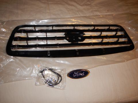 2003 Ford Crown Victoria - black-and-chrome front grille with a hardware bag and a blue Ford oval emblem arranged on a white sheet.