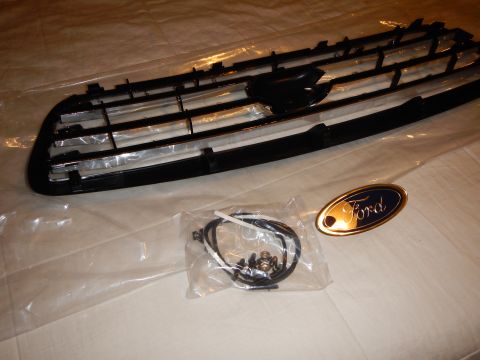 2003 Ford Crown Victoria - Angled black-and-chrome grille with a hardware bag and a gold-rimmed blue Ford oval emblem on a white sheet.