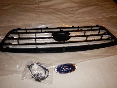 2003 Ford Crown Victoria - black-and-silver bar grille with a hardware bag and a blue Ford oval emblem laid out on a white sheet.