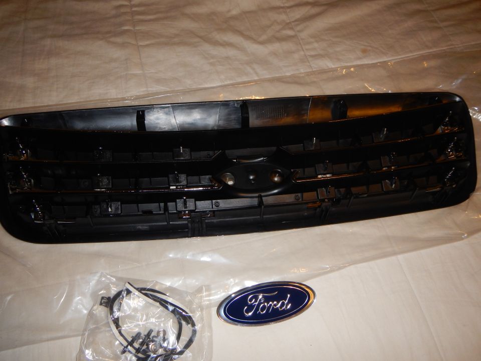 Rear of black-and-chrome grille with mounting clips, hardware bag and blue Ford oval