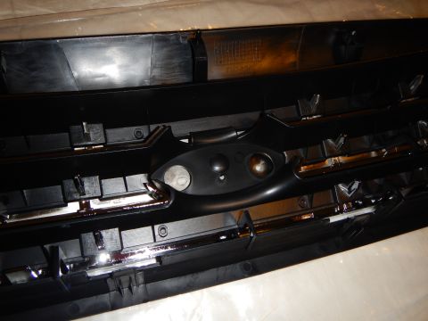 2003 Ford Crown Victoria - Close-up of the rear of a black plastic automotive grille, showing molded mounting tabs, clips and the emblem mount housing.
