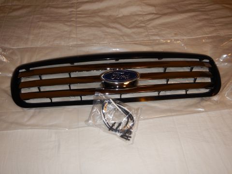 2003 Ford Crown Victoria - black automotive grille with chrome bar accents and a blue Ford oval emblem, displayed with a bagged wiring harness and screws.