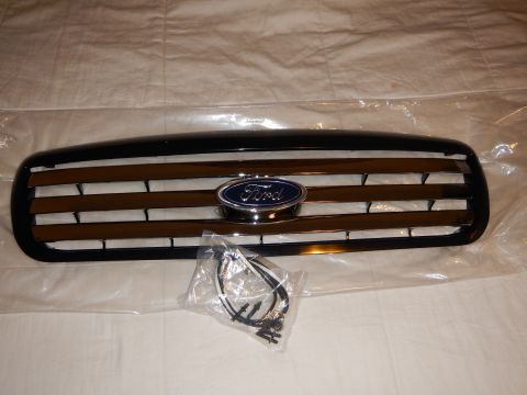 2003 Ford Crown Victoria - Front view of a black Ford grille with chrome horizontal bars and a centered blue oval emblem, shown with a bagged wiring harness.