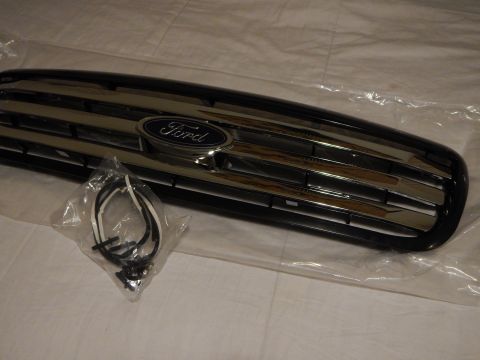 2003 Ford Crown Victoria - Angled close view of a black Ford grille showing the blue oval emblem and chrome horizontal bars, with a bagged harness in front.