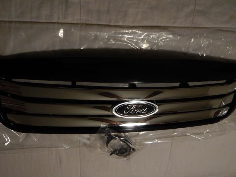 2003 Ford Crown Victoria - dimly lit close-up of a black Ford grille showing chrome horizontal bars and the blue oval emblem, with a harness bag below.