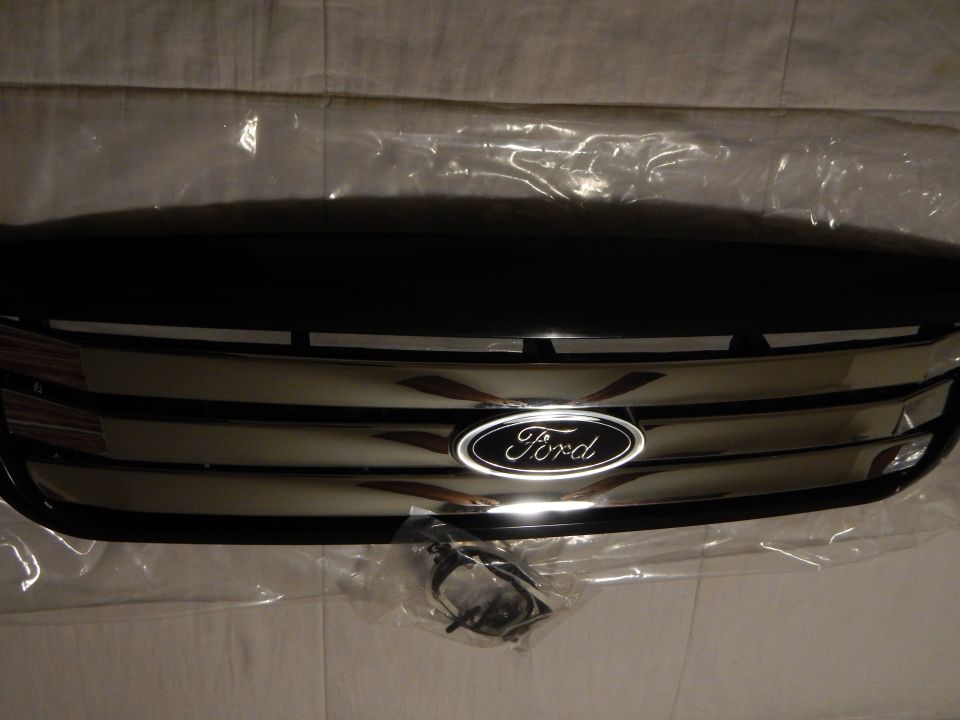 Dim close-up of black Ford grille with chrome bars and blue oval emblem
