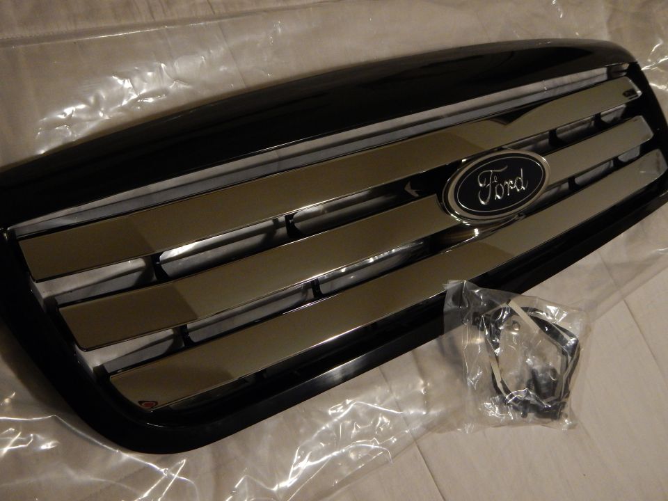 Angled black Ford grille with chrome bars and blue oval emblem and harness