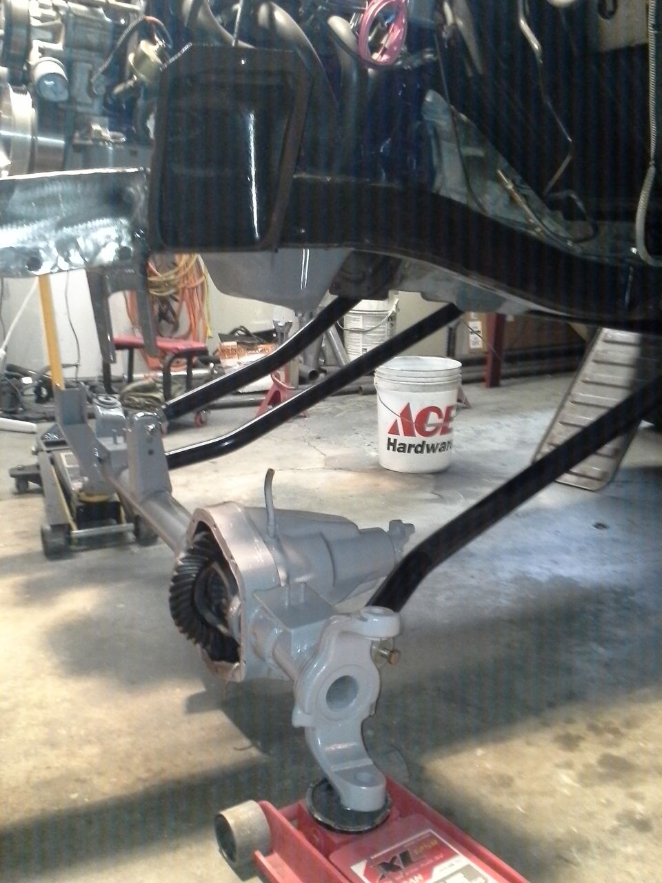 vehicle's front axle assembly, painted gray, supported by jacks in a garage