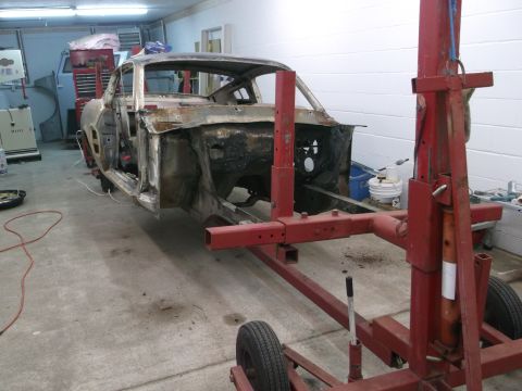 1967 Ford Mustang - A heavily damaged 1967 Ford Mustang body shell is supported by a red frame machine in a garage.