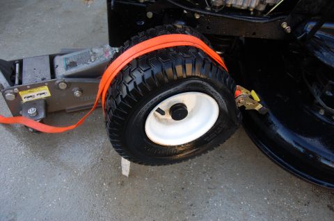 2006 Honda RANCHER - A lawn mower wheel is strapped to a jack, suggesting maintenance or repair.