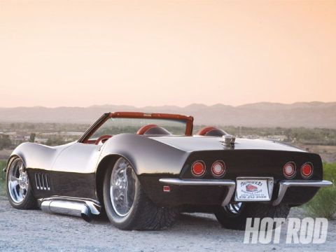 1976 Chevrolet Corvette - A black convertible sports car with a red interior is parked outdoors with mountains in the background.