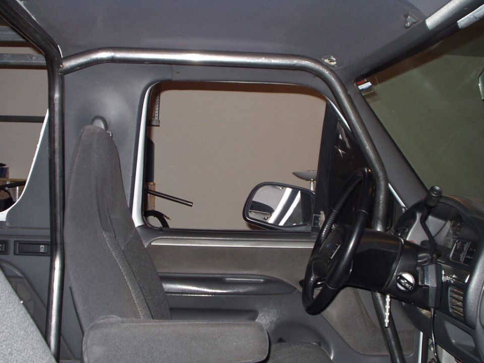 Vehicle interior with gray seat, roll cage tubing, side mirror, and right-hand-drive steering wheel