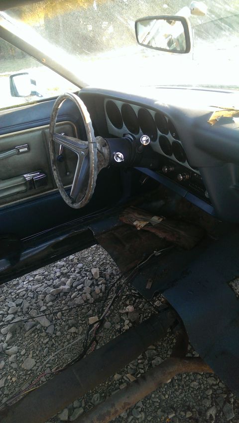 1975 Ford Ranchero - The interior of a 1975 Ford Ranchero shows a dashboard with multiple oval gauges and a worn steering wheel.