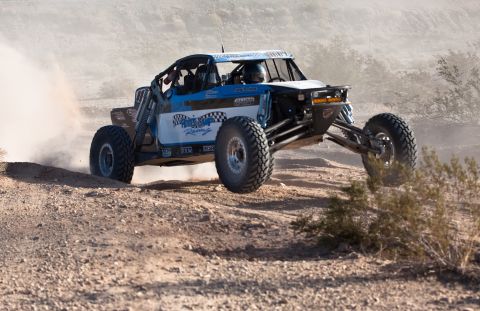 1996 Ford Bronco - Off-road buggy races through a dusty desert landscape, its large tires kicking up plumes of dirt.