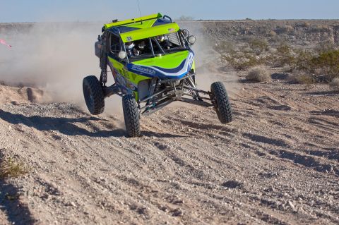 1996 Ford Bronco - An off-road buggy jumps over a dirt mound during a race.