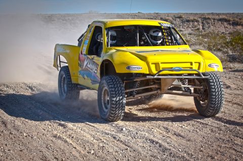 1996 Ford Bronco - Off-road race truck with drivers in helmets navigates a dusty desert course.
