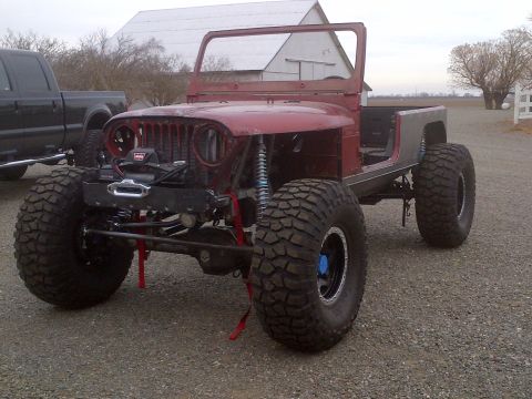 1985 Jeep CJ7 - This modified Jeep CJ-series is shown with oversized tires and a winch, alongside a pickup truck.