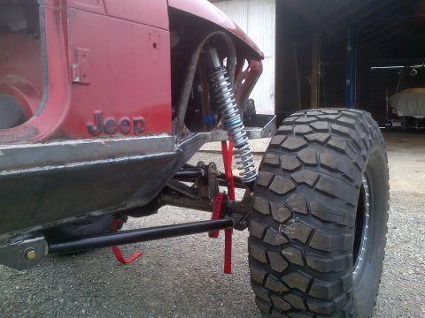 1985 Jeep CJ7 - Custom off-road Jeep build showing suspension and large tire. The vehicle is in a workshop.