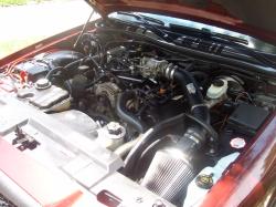 2004 Ford Crown Victoria - The engine bay of a red vehicle is shown, an aftermarket air intake system and various engine components.