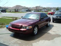 2004 Ford Crown Victoria - A maroon 2004 Ford Crown Victoria is parked on a driveway with other vehicles visible in the background.