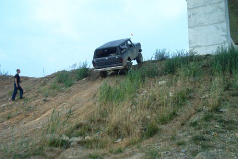 1979 Ford Bronco - A person watches a 1979 Ford Bronco ascend a steep, grassy incline near a large concrete pillar.