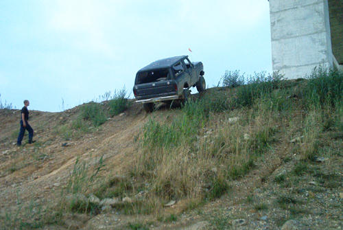 Dark muddy Ford Bronco perched on a steep dirt embankment with a person walking below