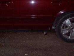 2004 Ford Crown Victoria - The side profile of a red vehicle is visible, with a focus on the rear wheel and a portion of the exhaust system.
