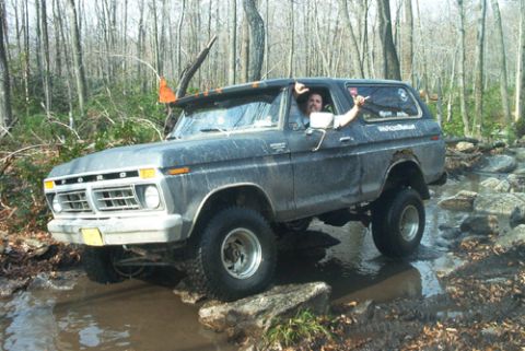 1979 Ford Bronco - A driver navigates a dark gray 1978 Ford Bronco through a rocky, watery trail in a wooded area.