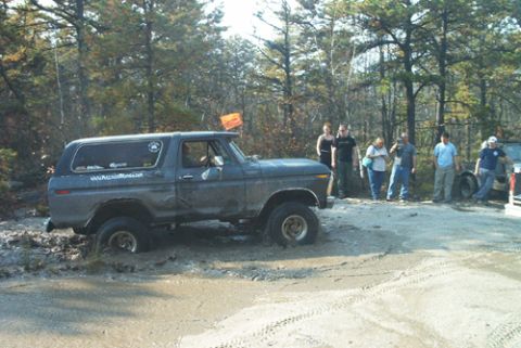 1979 Ford Bronco - A 1979 Ford Bronco navigates a muddy trail, with a group of onlookers observing the off-road adventure.