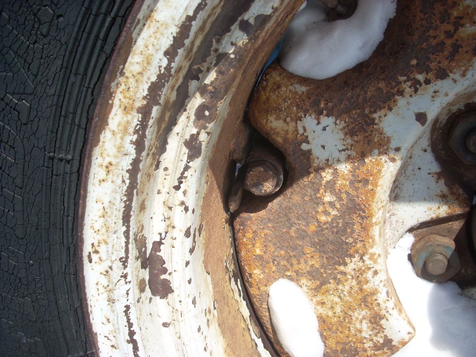 Close-up of a rusty wheel hub with peeling white paint and a cracked black tire
