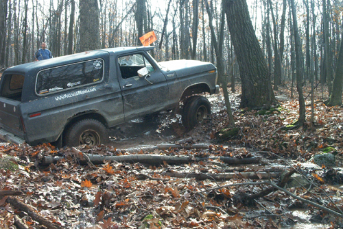 Muddy blue Bronco with white top on a leaf-covered woods trail
