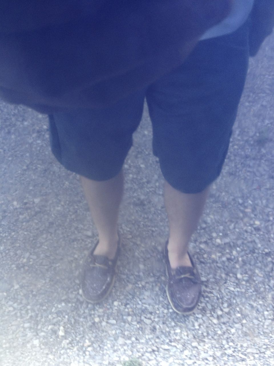 person wearing shorts and loafers standing on gravel