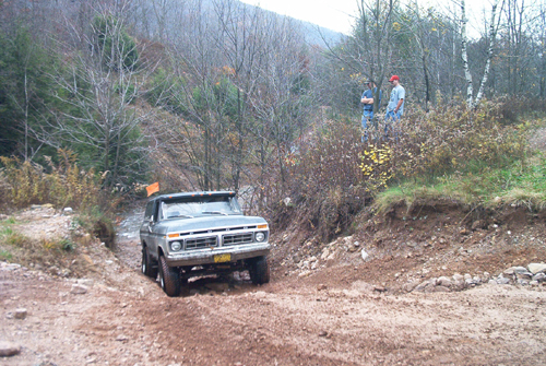 Ford F-Series truck going off-road on a muddy trail with two people watching